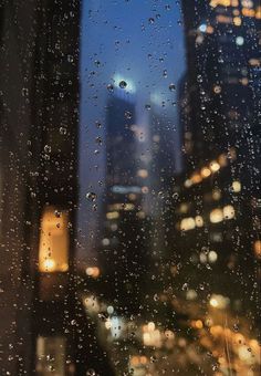 rain drops on the window and buildings in the background at night, with city lights lit up behind them