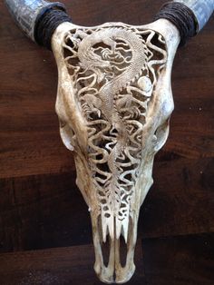 an animal skull with long horns and intricate carvings on it's back end, sitting on a wooden surface