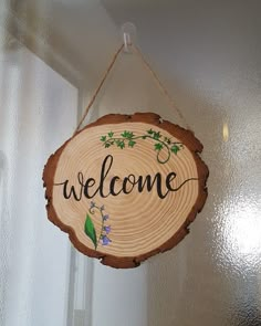 a welcome sign hanging from the side of a door with wood slices and flowers on it