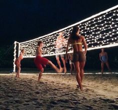 some people are playing volleyball on the beach at night with lights strung up behind them