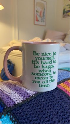 a coffee mug sitting on top of a bed next to a crocheted blanket