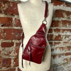 a white mannequin with a red leather purse on it's back and a brick wall in the background