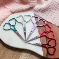 four pairs of scissors sitting on top of a cutting board next to a pink towel