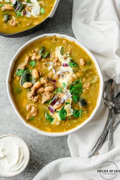 two bowls of soup with beans, spinach and sour cream on the side next to spoons