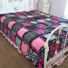 a bed with a pink, black and white quilt on it's cover in a bedroom