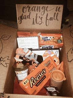 an open box filled with snacks and candy on top of a table next to a sign that says orange is glad it's fall