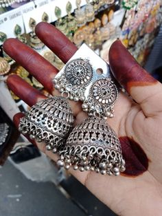 a person is holding three pairs of silver colored earrings in their hand and there are other jewelry on display behind them