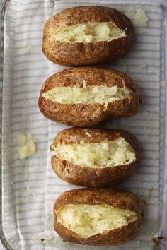 four baked potatoes sitting on top of a baking pan covered in butter and other toppings