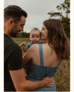 a man and woman holding a baby in their arms while standing in the middle of a field