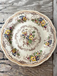 a white plate with flowers on it sitting on top of a wooden table next to a knife and fork