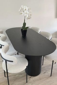 a black table surrounded by white chairs and a vase with flowers in it on the floor