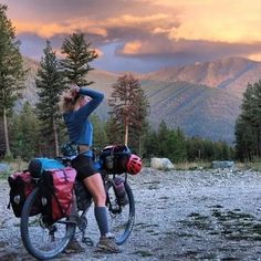 a woman is sitting on her bike in the wilderness with mountains and trees behind her