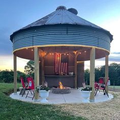 an outdoor fire pit with chairs around it and american flag on the wall behind it