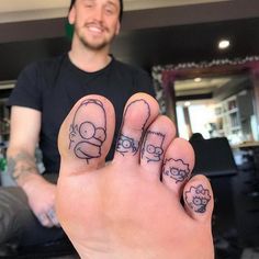 a hand with some tattoos on it and a person in the background holding up their fingers