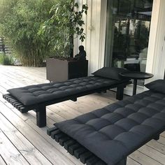 two black chaise lounges sitting on top of a wooden deck next to a planter