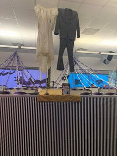 two suits and one dress hanging from the ceiling in an office setting with other items on display