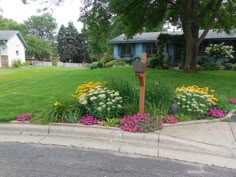 a yard with flowers and a mailbox in the foreground, next to a house