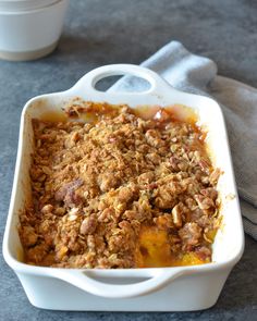 a casserole dish filled with fruit and crumbled toppings next to a cup of coffee