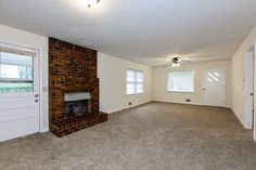 an empty living room with brick fireplace and white doors in the corner, on carpeted floor