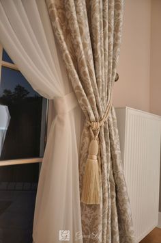 curtains with tassels hanging from them in front of a window that has a white radiator