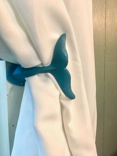 a curtain with a blue bird on it's side hanging from a hook in front of a white curtain