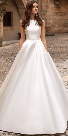 a woman in a white wedding dress standing on a cobblestone street with her hands behind her back