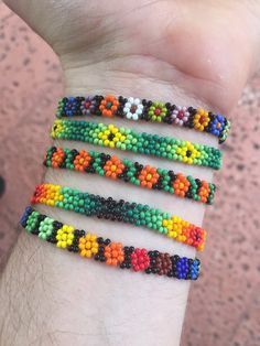 four bracelets with different colors and designs on the wrist, all made out of seed beads