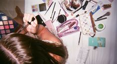 a woman laying on top of a table covered in makeup and other cosmetics items,