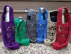 four different colored crocheted purses sitting next to each other on the ground