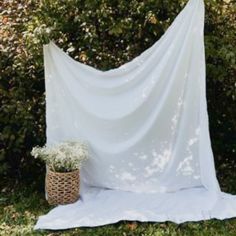 a white cloth draped over a basket with flowers in front of it on the grass