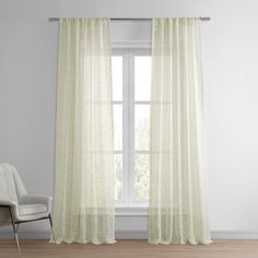 a white chair sitting in front of a window next to a pair of sheer curtains