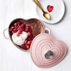 a heart - shaped dish with strawberries and whipped cream in it next to a pink pot