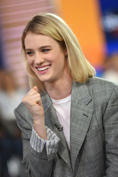 a woman with blonde hair smiling and holding her fist up in the air while wearing a blazer