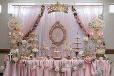 a table topped with lots of cakes and desserts next to a wall covered in pink drapes