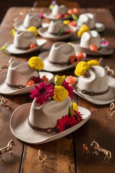 several white hats with flowers on them sitting on a wooden table next to toy horses