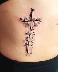 a cross tattoo on the side of a woman's stomach, with flowers growing out of it