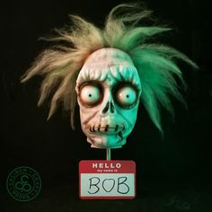 a creepy mask with green hair and eyes on top of a sign that says hello bob