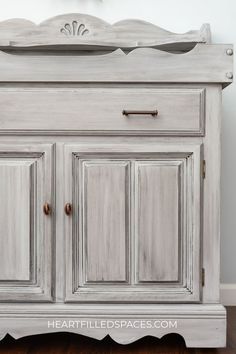 an old dresser painted in white with wood trimmings and gold hardware on top