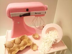 a pink mixer sitting on top of a table next to an egg shell and other items