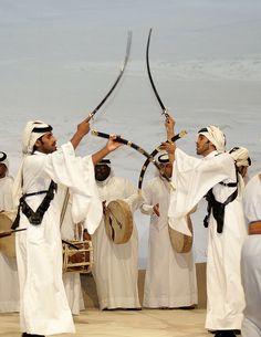 a group of men in white outfits holding up two large swords while standing next to each other