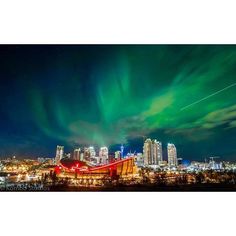 an aurora bore over the city at night with green and red lights in the sky