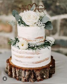 a wedding cake with white flowers and greenery is on top of a tree stump