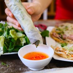 a person holding a vegetable spring roll over a plate of salad and other food items