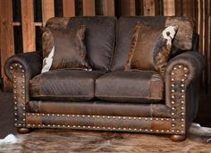 a brown leather couch with cow hide pillows on it's back and two cows