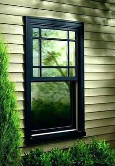 an open window on the side of a house in front of some bushes and trees