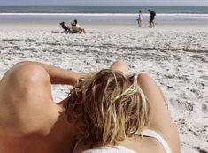 a woman laying on top of a sandy beach next to the ocean with people in the background