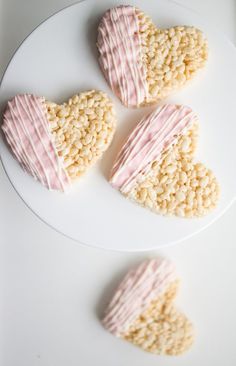 three heart shaped cookies sitting on top of a white plate next to each other with pink icing