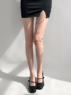 a woman with tattoos on her legs wearing black high heels and a skirt, standing in front of a white wall