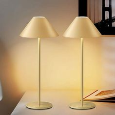 two lamps sitting on top of a white table next to a book and lamp shade