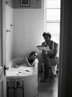 black and white photograph of two people in a bathtub, one reading a book